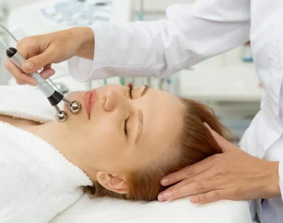 A professional therapist performing microcurrent facials using dual probes to lift and tone the facial muscles of a client for a natural contouring effect.